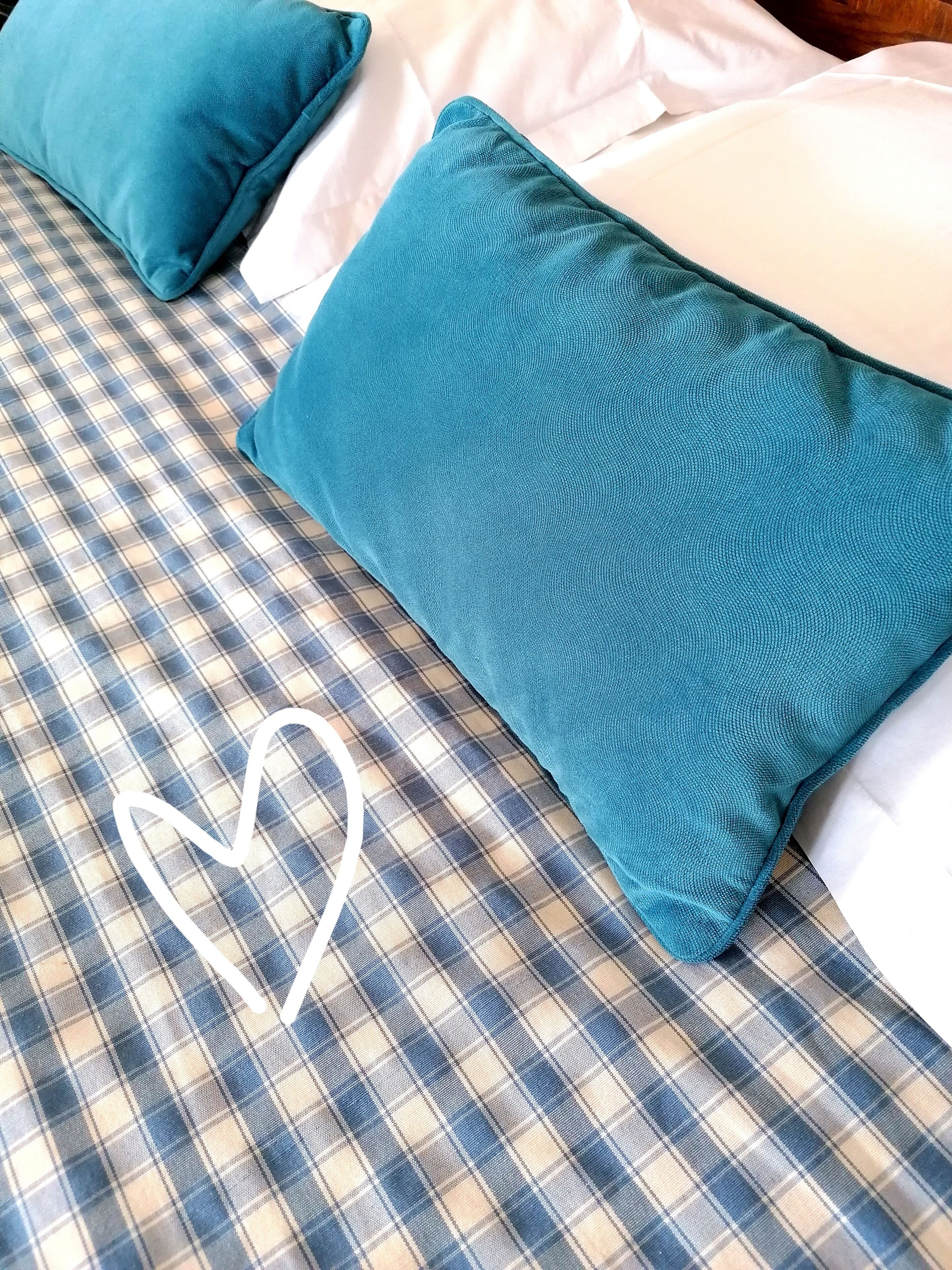Un letto con una coperta a quadri e due cuscini color petrolio.