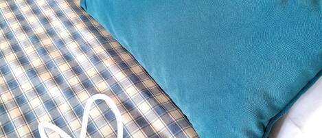 Una cama con colcha escocesa y dos almohadas color turquesa.