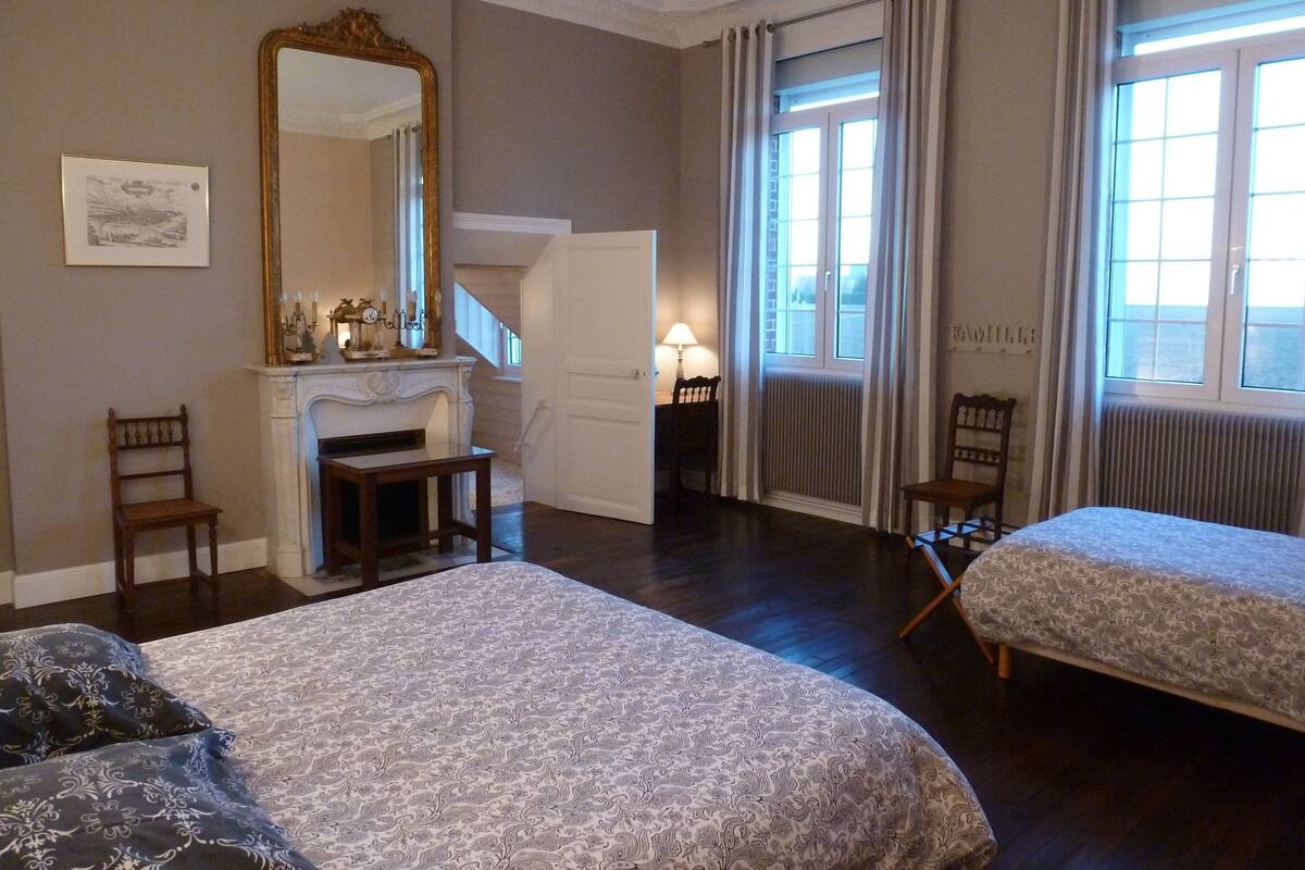 A hotel room with two beds, a fireplace, a large mirror, and a view of the sea through the windows.