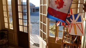 A room with a large window, a wooden chair, and a flag rack with multiple flags. - Ferme de Bonavis - Chambres d'Hôtes (Banteux)