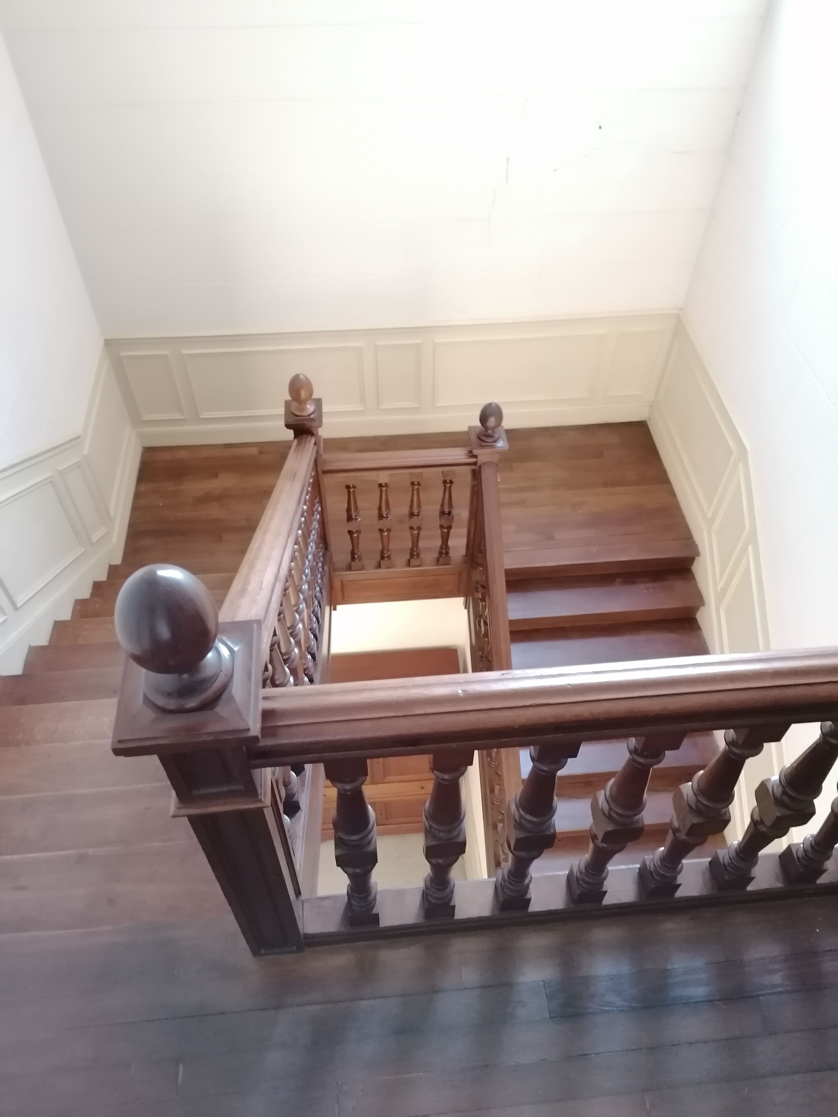 A wooden staircase with a handrail and balusters, leading to an upper floor.