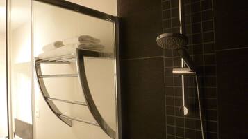 A modern bathroom with a glass shower enclosure, a towel rack with folded towels, and a showerhead.