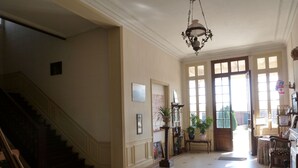 A spacious hallway with a staircase, a chandelier, and large windows allowing natural light. - Ferme de Bonavis - Chambres d'Hôtes (Banteux)