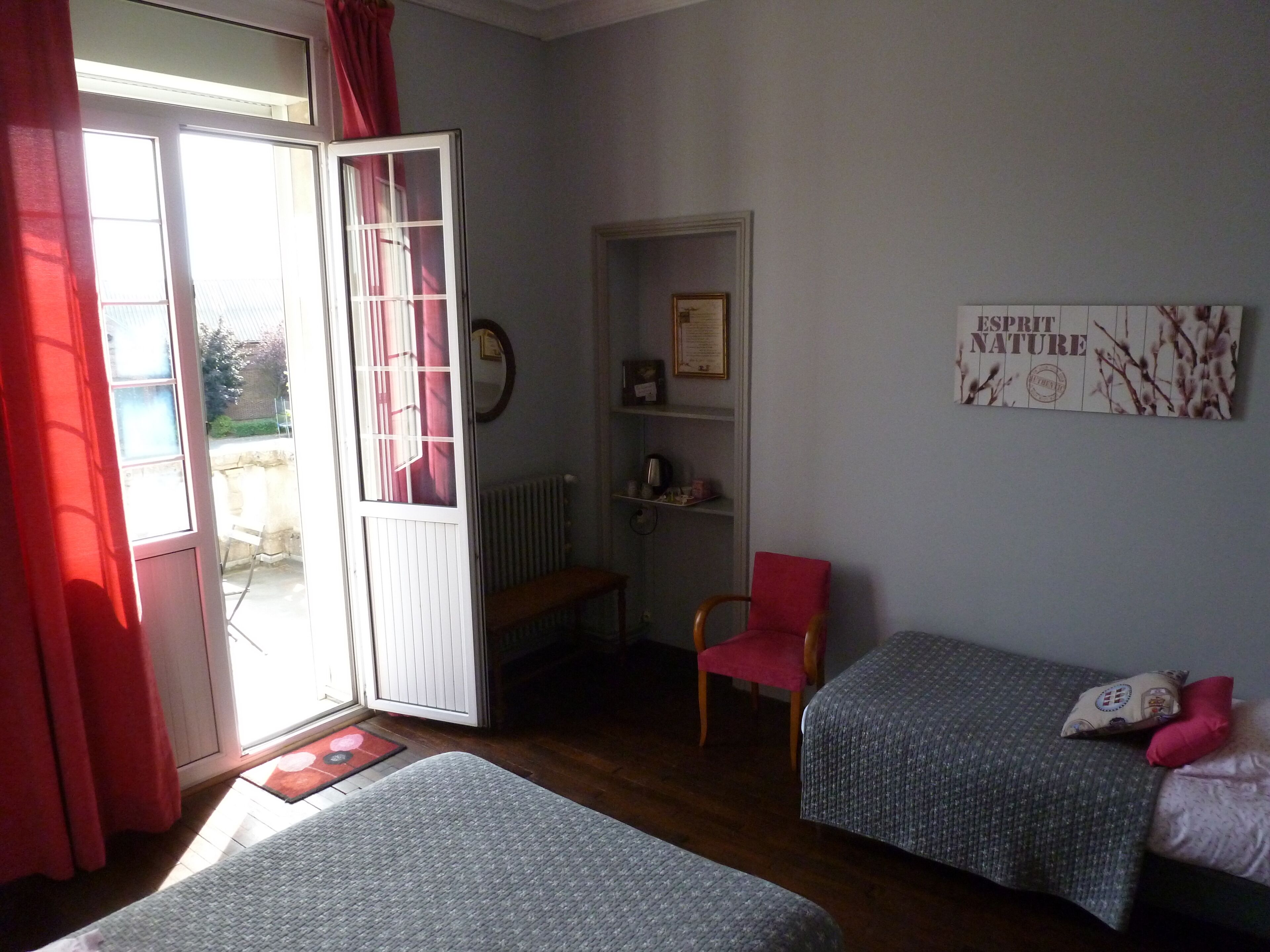 A room with two beds, a chair, a radiator, and a wall with a framed certificate.