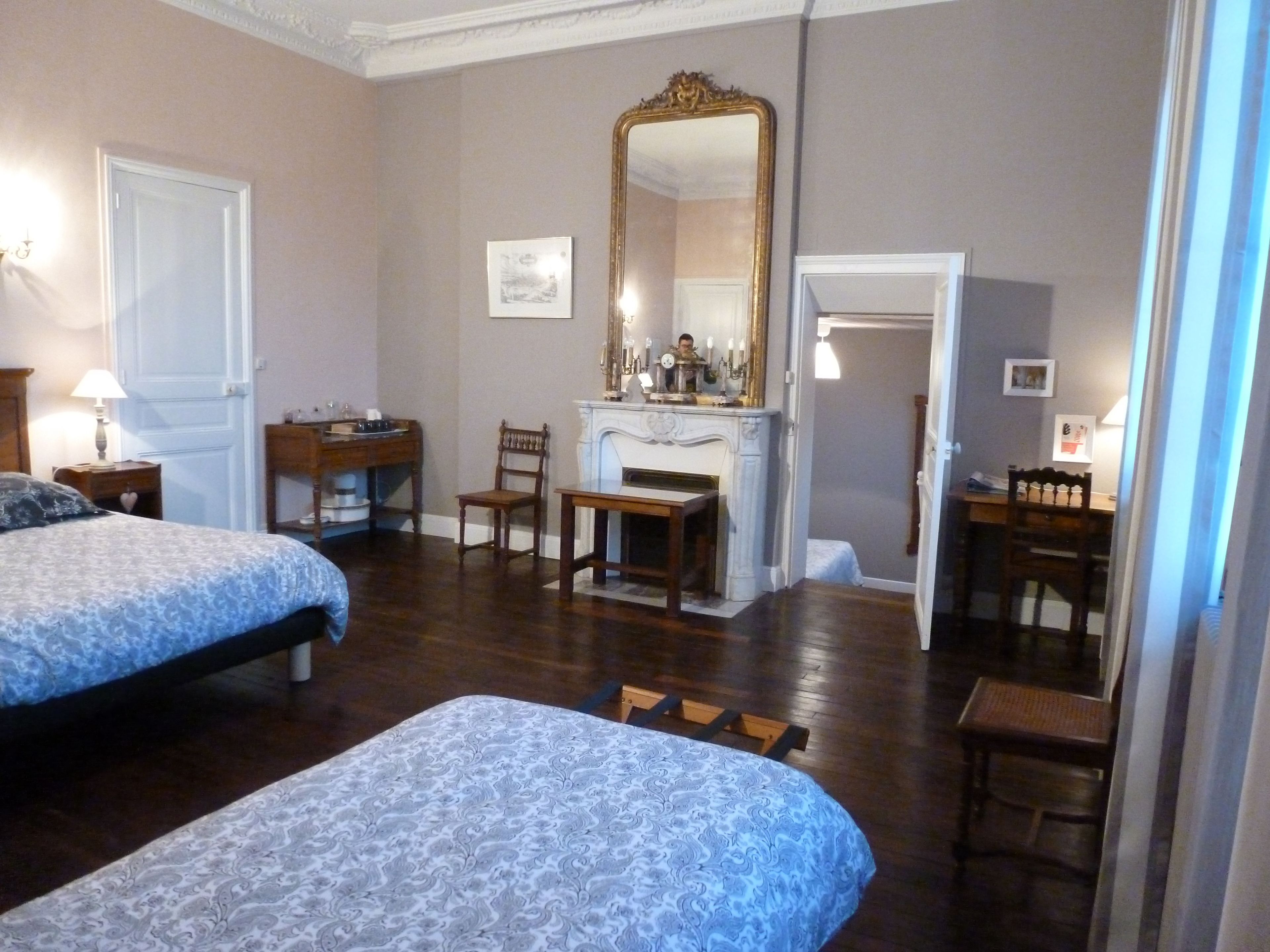 Een hotelkamer met twee bedden, een bureau, een stoel, een open haard en een grote spiegel.