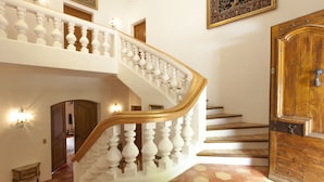 Een statige trap met witte balustrades en een gouden leuning, die leidt naar een houten deur met een messing knop.
