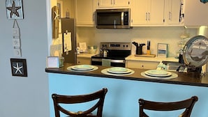 A kitchen with white cabinets, a microwave, an oven, and two wooden chairs.