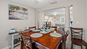A dining area with a wooden table, chairs, and a ceiling fan. There is a painting on the wall and a sign that reads "Seaside".
