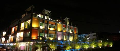 A multi-story building with balconies and a parking area in front.