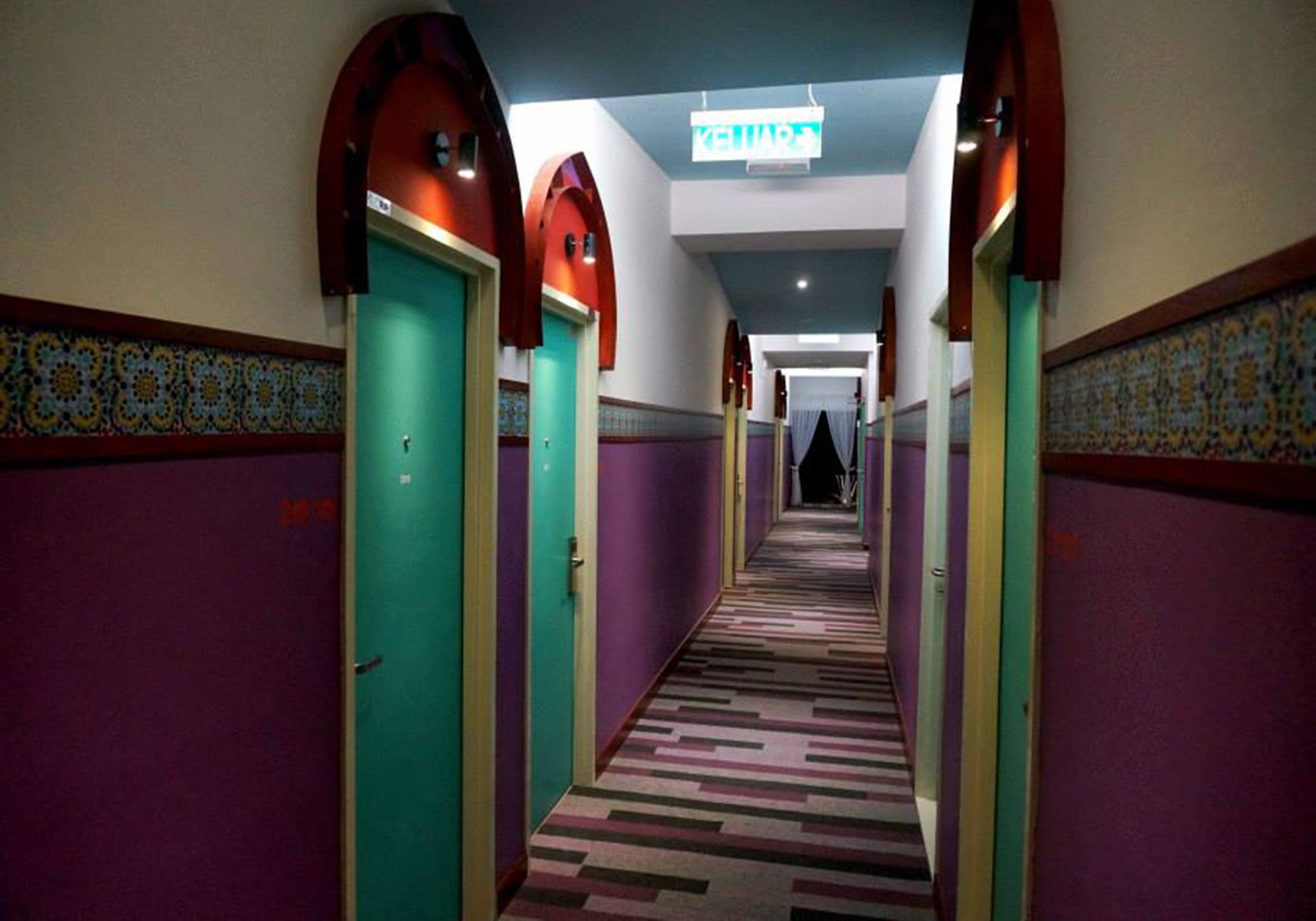 A hotel hallway with purple walls, green doors, and a patterned carpet.