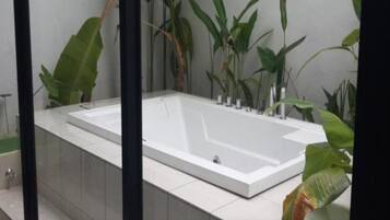 Un baño moderno con una bañera rectangular grande, paredes con azulejos y plantas verdes de gran tamaño.