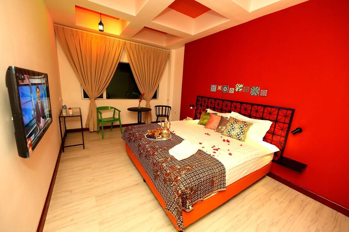 Quarto com cama, televisão, secretária e cadeira.