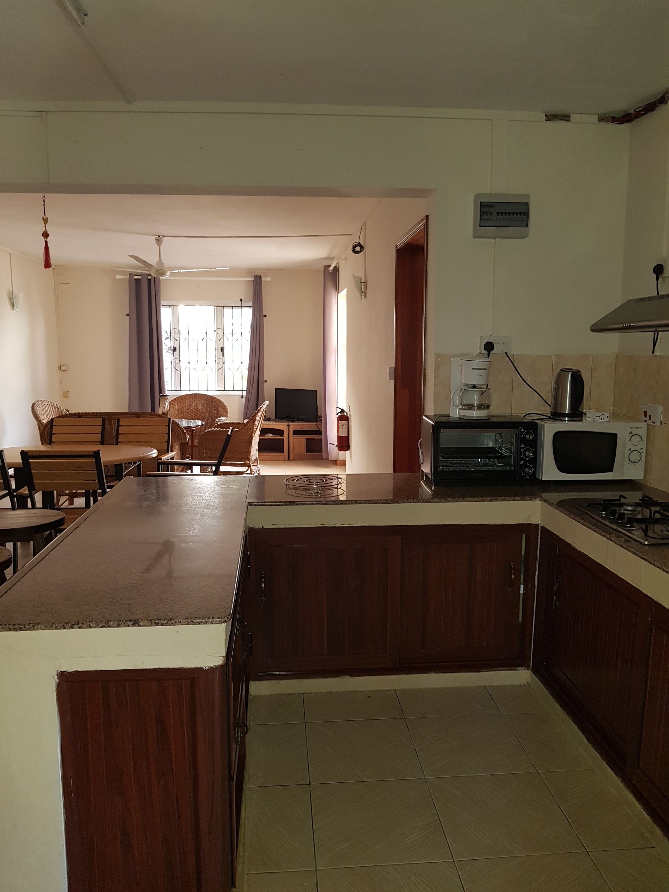 Una cocina con una isla central, un comedor con banco y un televisor al fondo.