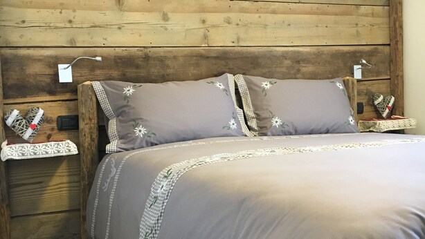 A wooden headboard with a checkered pillow and a grey bedspread. - Atmosphere di Montagna (Vermiglio)