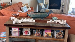 Una sala de estar con chimenea, un televisor montado encima y un sofá con cojines. Hay objetos decorativos sobre una mesa de centro de madera, y cestas en un mueble debajo.