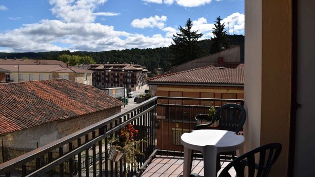 A balcony with a table and chairs, overlooking a town with terracotta-roofed buildings and a clear sky. - Hostal La Tablada (Navaleno)