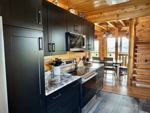 A modern kitchen with dark cabinetry, a granite countertop, and a dining area with wooden furniture. - HEAVENLY DAZE — THREE KING SUITES, THREE LIVING AREAS & ROOM FOR 12 (Sevierville)