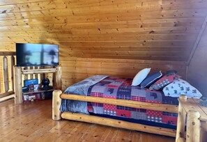 Une cabane en bois avec un lit, une télévision et une petite table sur laquelle se trouvent des livres et un globe terrestre.