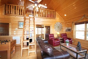 A wooden cabin interior with a loft bedroom, a foosball table, leather seating, and a dartboard. - HEAVENLY DAZE — THREE KING SUITES, THREE LIVING AREAS & ROOM FOR 12 (Sevierville)