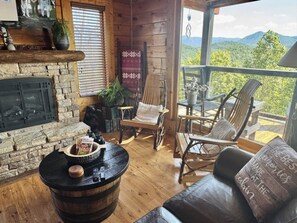 Un intérieur de chalet chaleureux avec une cheminée en pierre, des meubles en bois et une vue sur les montagnes.