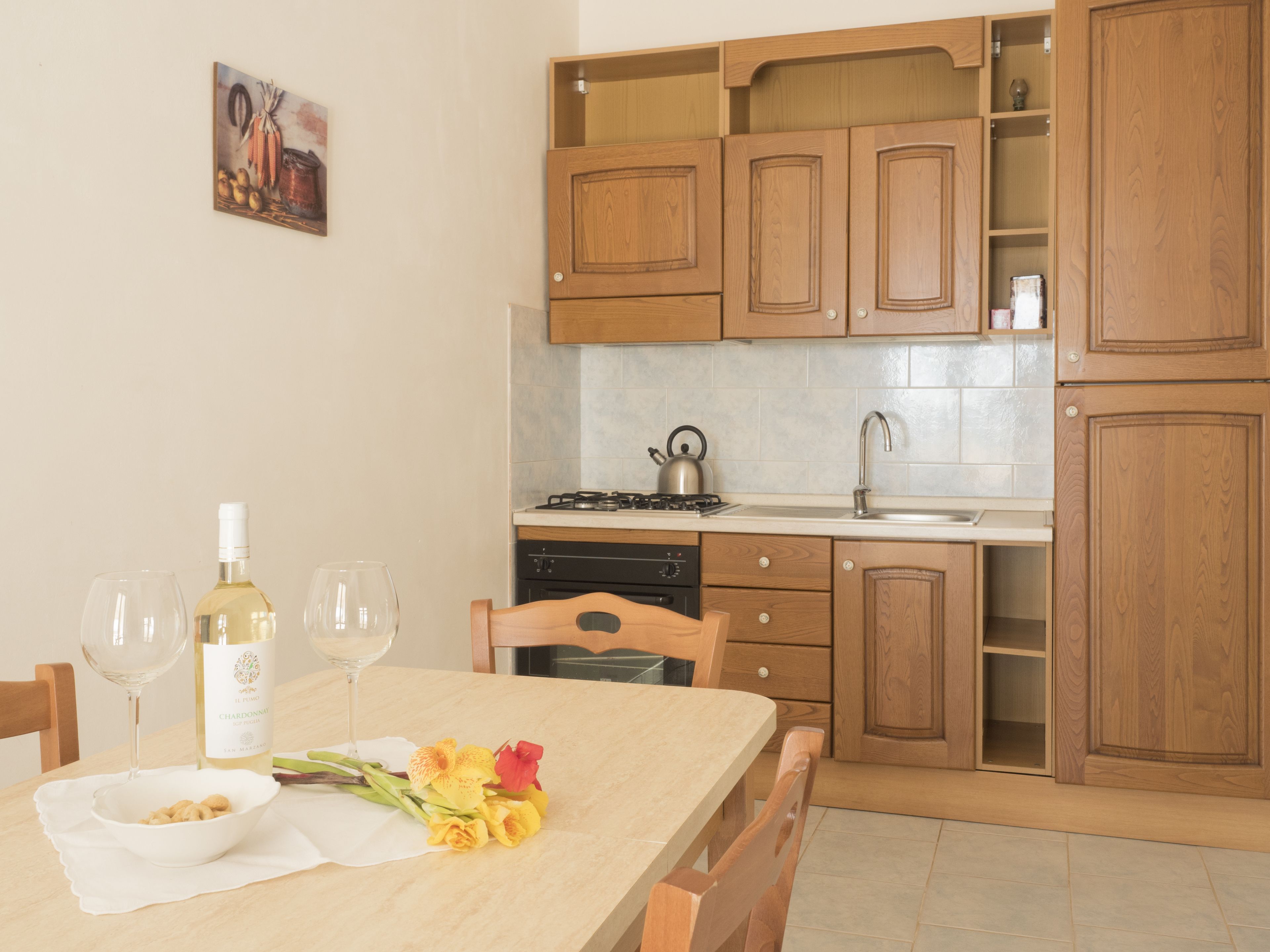 Una cocina con armarios de madera, una estufa y un lavamanos. Hay una mesa de comedor con un tazón de nueces, una botella de vino y vasos.