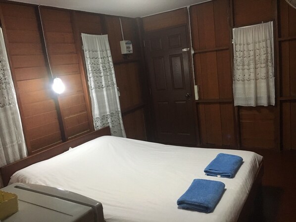 A hotel room with a bed, two blue towels, wooden panel walls, a door, and a window with a curtain.