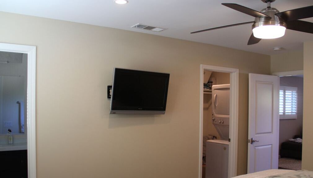 Une chambre dotée d’un ventilateur de plafond, d’un téléviseur fixé au mur et d’un placard dont la porte est entrouverte.