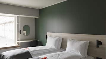 A modern hotel room with two beds, a desk, a mirror, and a window with a view of buildings.