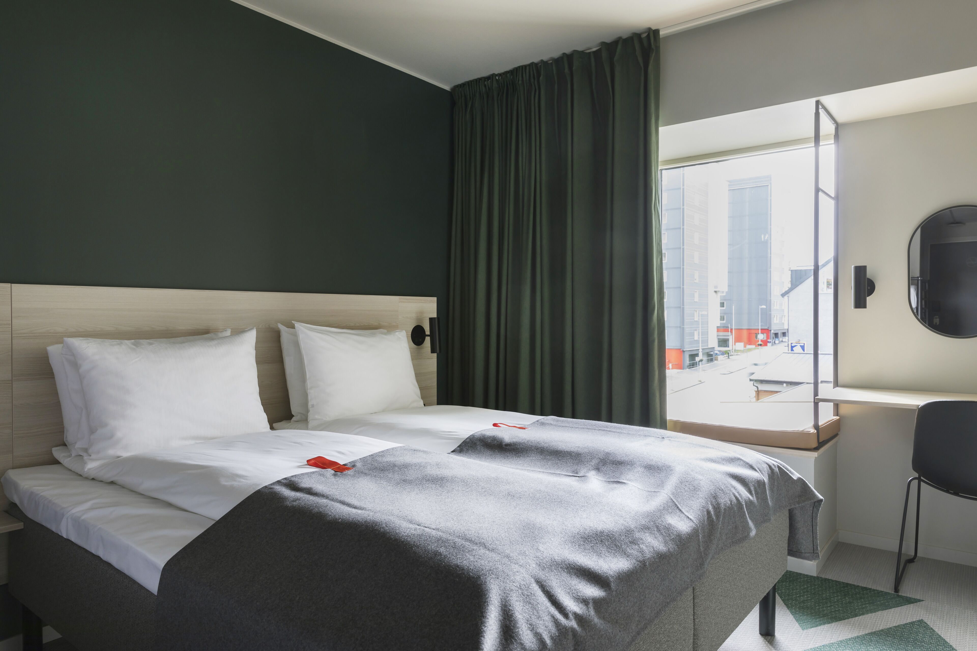A hotel room with a bed, a desk, and a window with curtains.