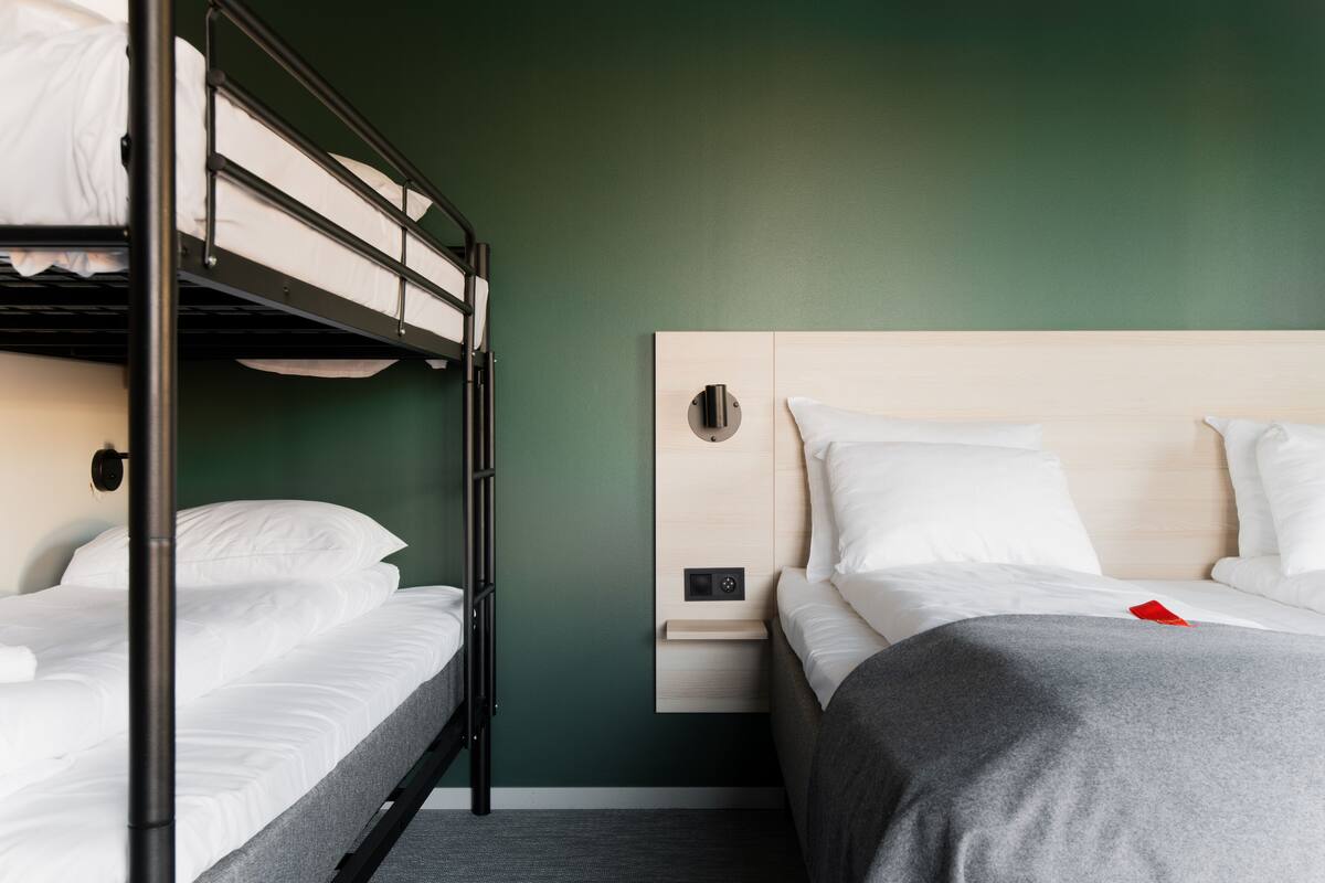 Habitación de hotel con literas, una mesita de noche y una mesilla auxiliar.