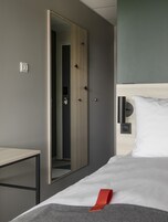 A modern hotel room with a bed, a bedside table, a wardrobe, and a mirror.