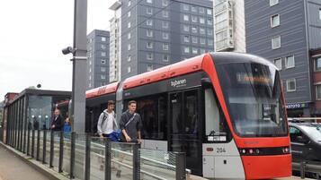 A modern train station with a red and black train, glass barriers, and urban buildings in the background.
