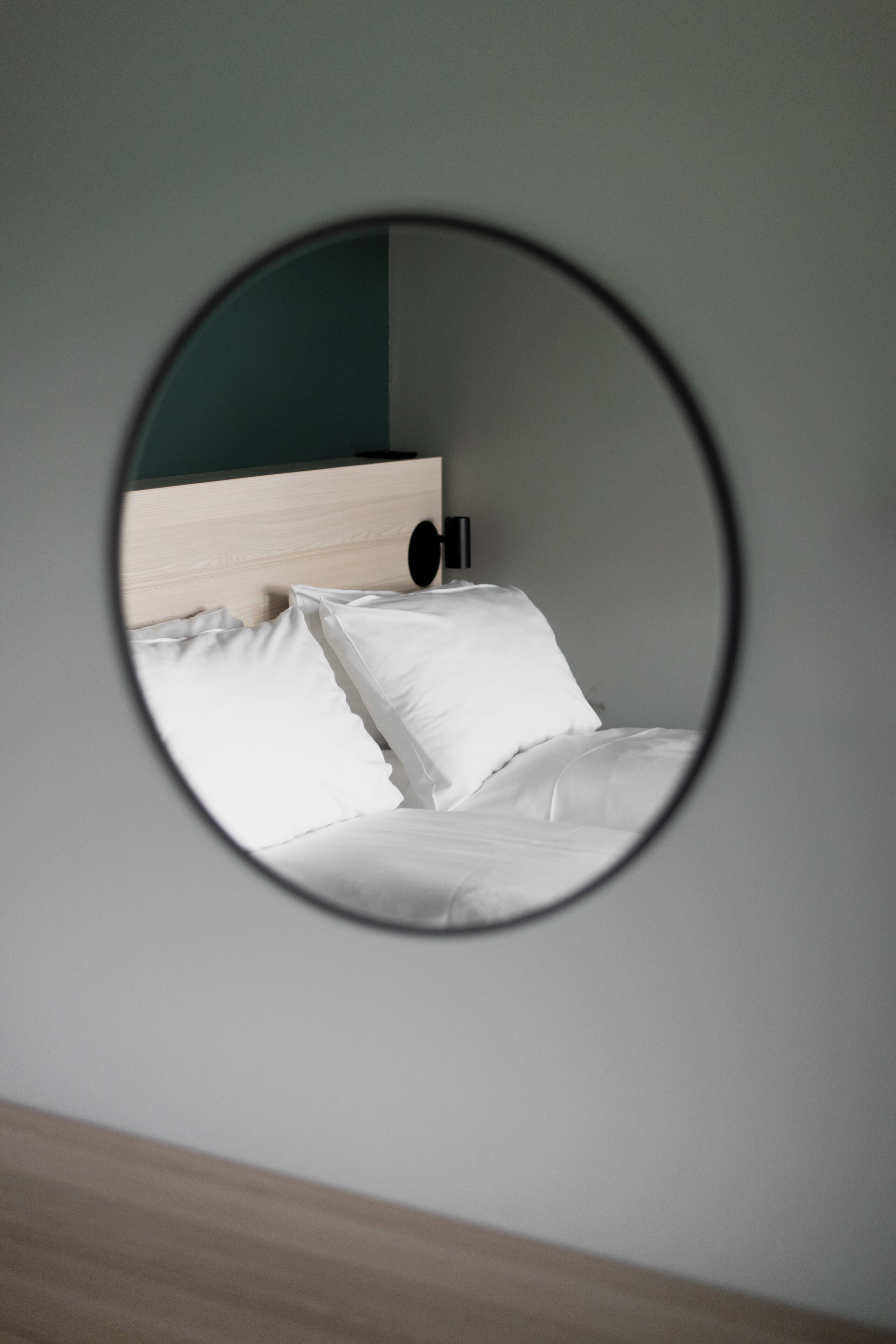 A bed with white bedding and a wooden headboard, viewed through a circular mirror.