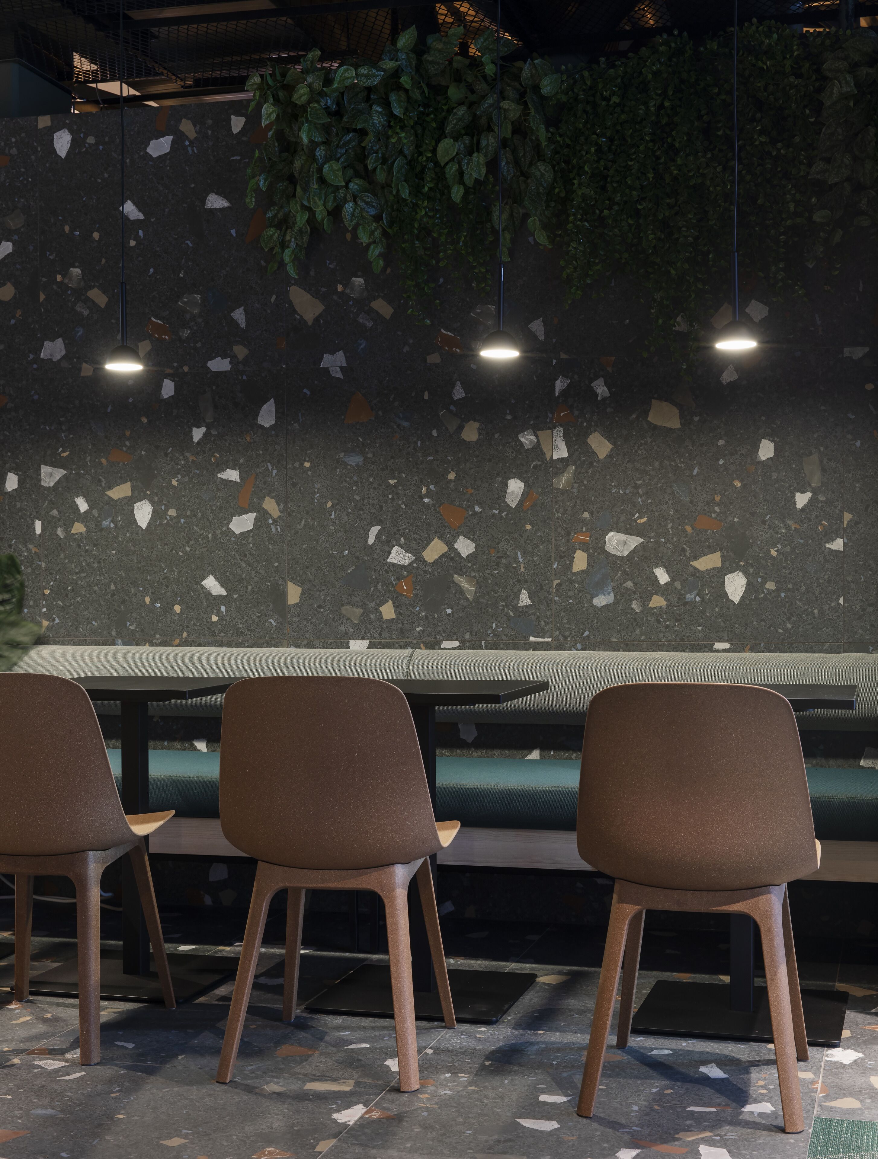 A seating area with three chairs and a table, a terrazzo floor, and a wall with a mosaic pattern.