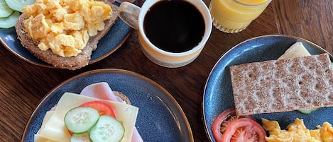 A breakfast setting with toast, scrambled eggs, ham, cheese, tomatoes, cucumbers, and grapes on plates, along with a cup of coffee and a glass of orange juice.
