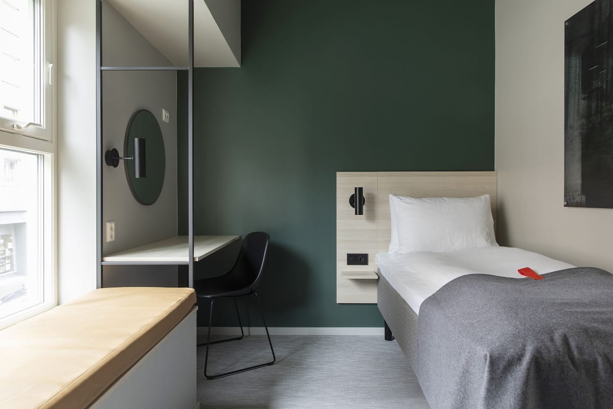 Habitación de hotel moderna con escritorio, silla, cama y un ventanal grande.