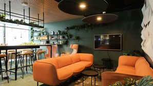 A modern lounge area with orange sofas, a bar with stools, and shelves with plants. - Citybox Bergen Danmarksplass (Bergen)