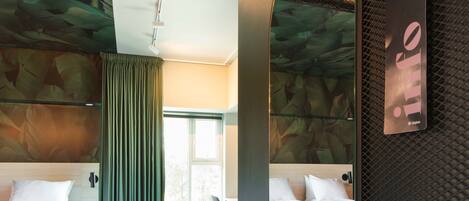 Habitación de hotel con dos camas, un espejo grande, una cortina verde y vistas al exterior.