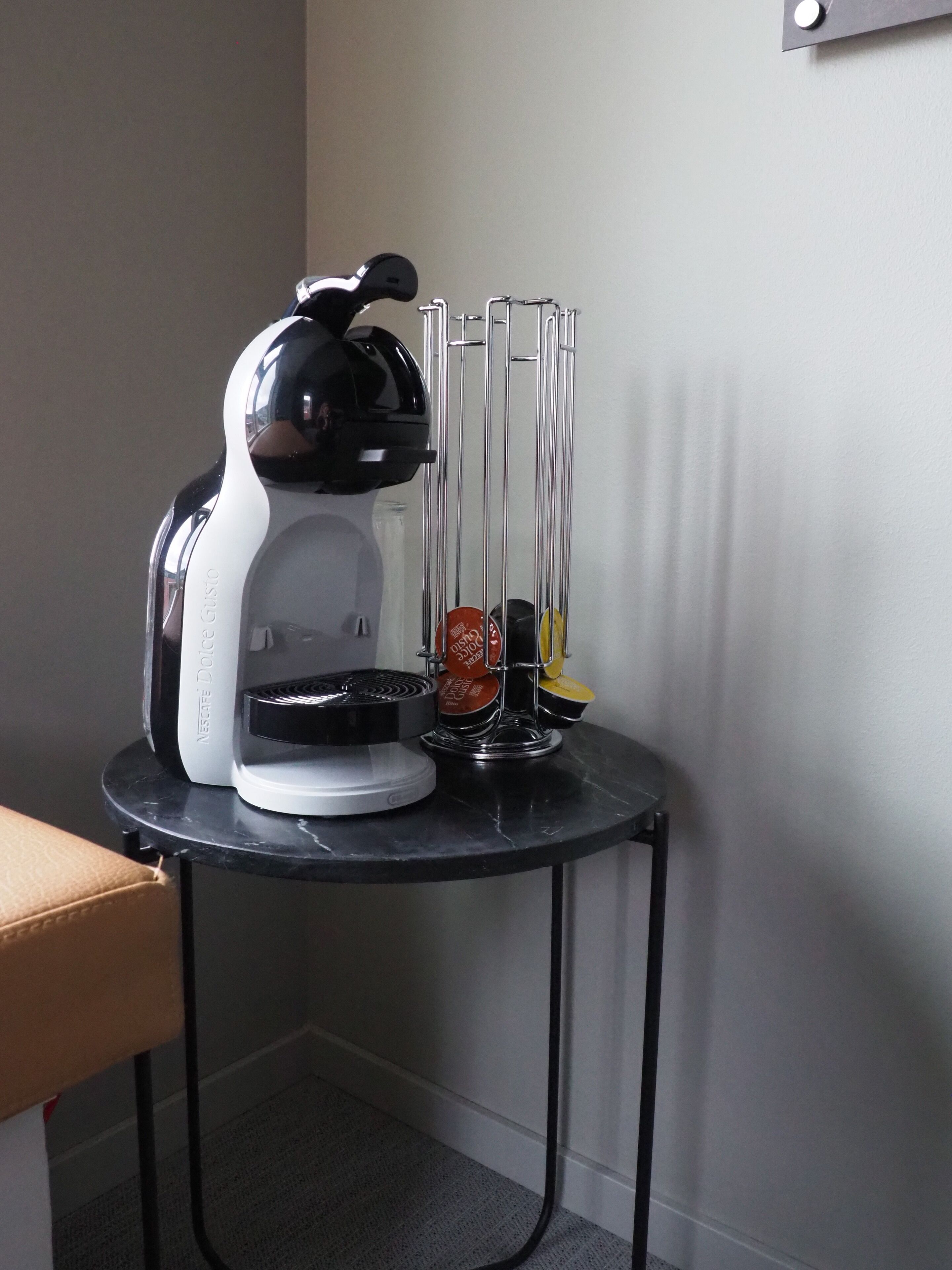 Una máquina de café Nespresso sobre una pequeña mesa, con una jarra de vidrio y un soporte metálico para cafetera.