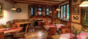 A cozy restaurant with wooden tables and chairs, stained glass windows, and a clock on the wall. - Lenzkircher Hof (Lenzkirch)