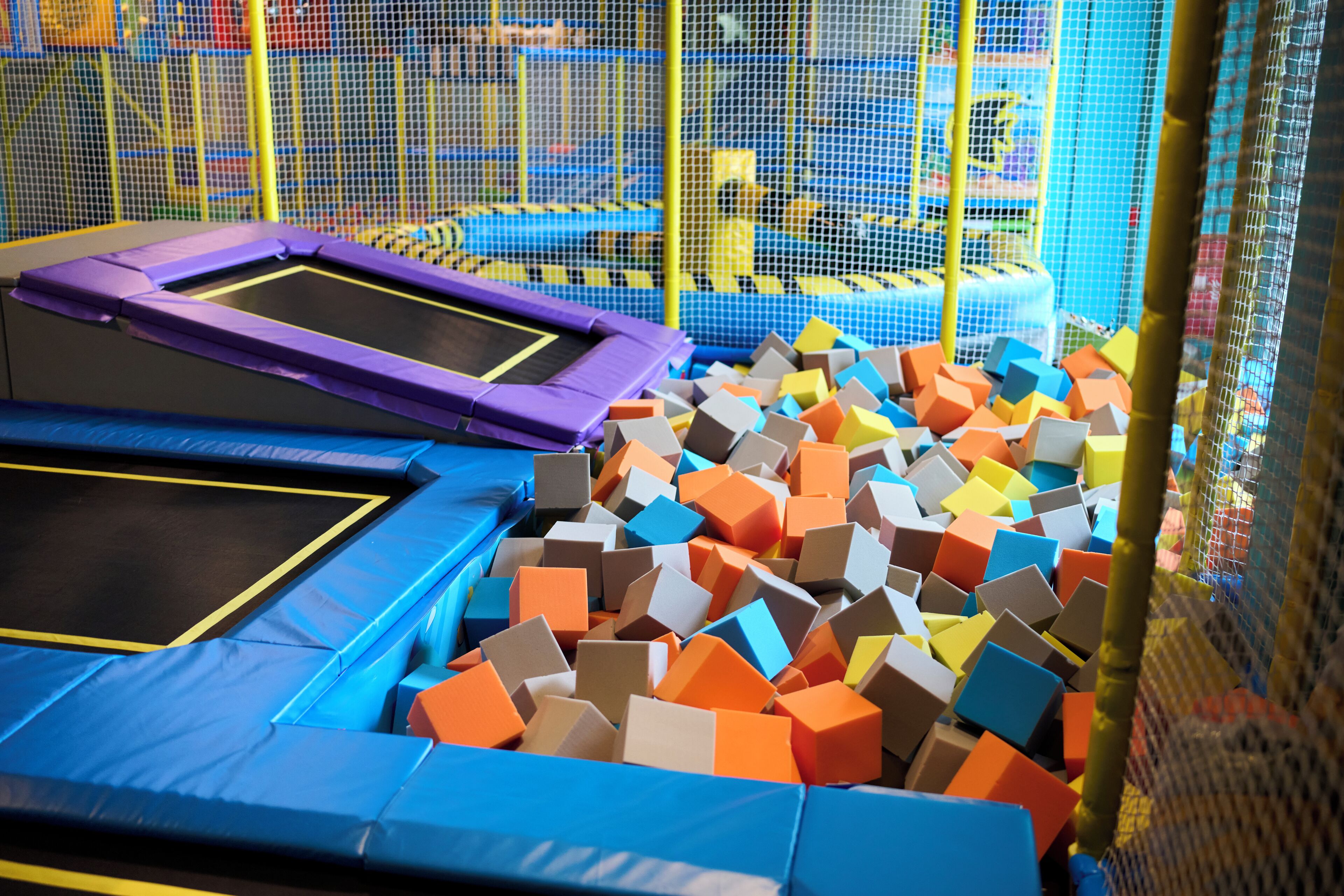 Un espace trampoline comprenant plusieurs trampolines et une fosse remplie de cubes de mousse de différentes couleurs.