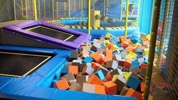 Un espace trampoline comprenant plusieurs trampolines et une fosse remplie de cubes de mousse de différentes couleurs.