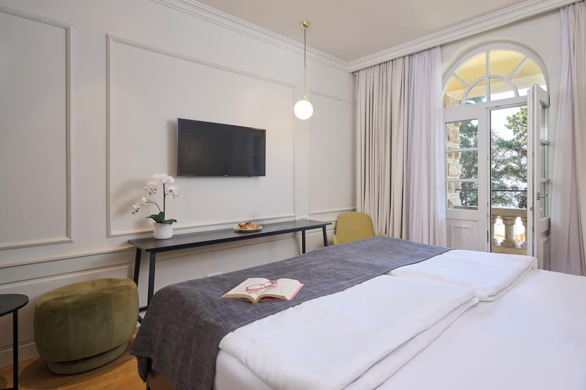 A hotel room with a bed, a desk, a chair, a TV, and a window with curtains.