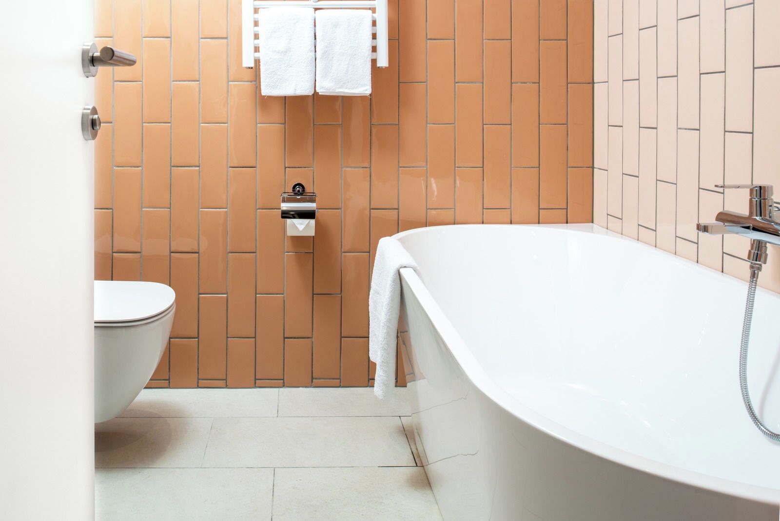 A modern bathroom with a white bathtub, a toilet, and a towel rack with two towels.