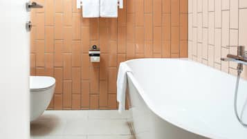 A modern bathroom with a white bathtub, a toilet, and a towel rack with two towels.
