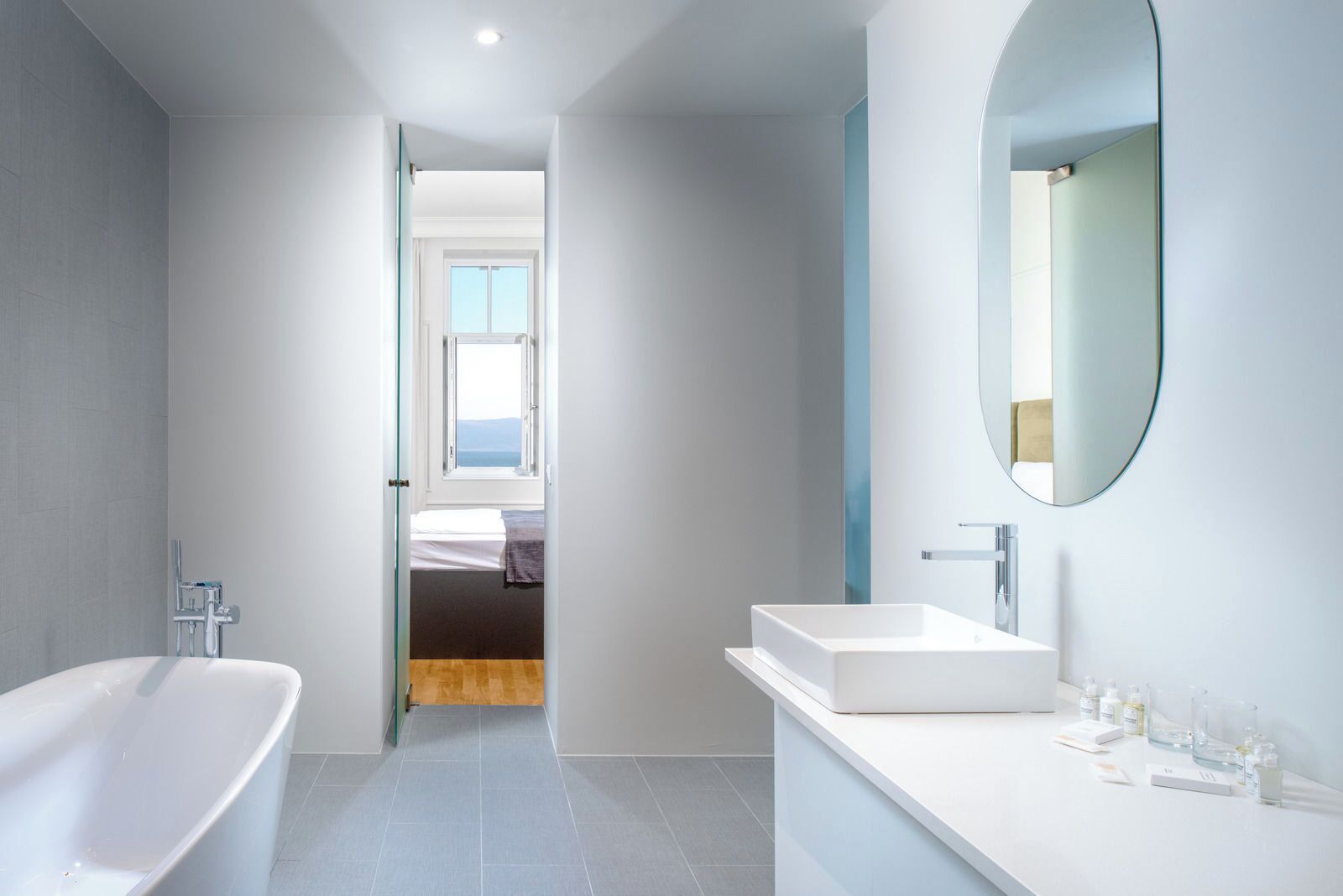 A modern bathroom with a freestanding bathtub, a large mirror, and a sink with toiletries.