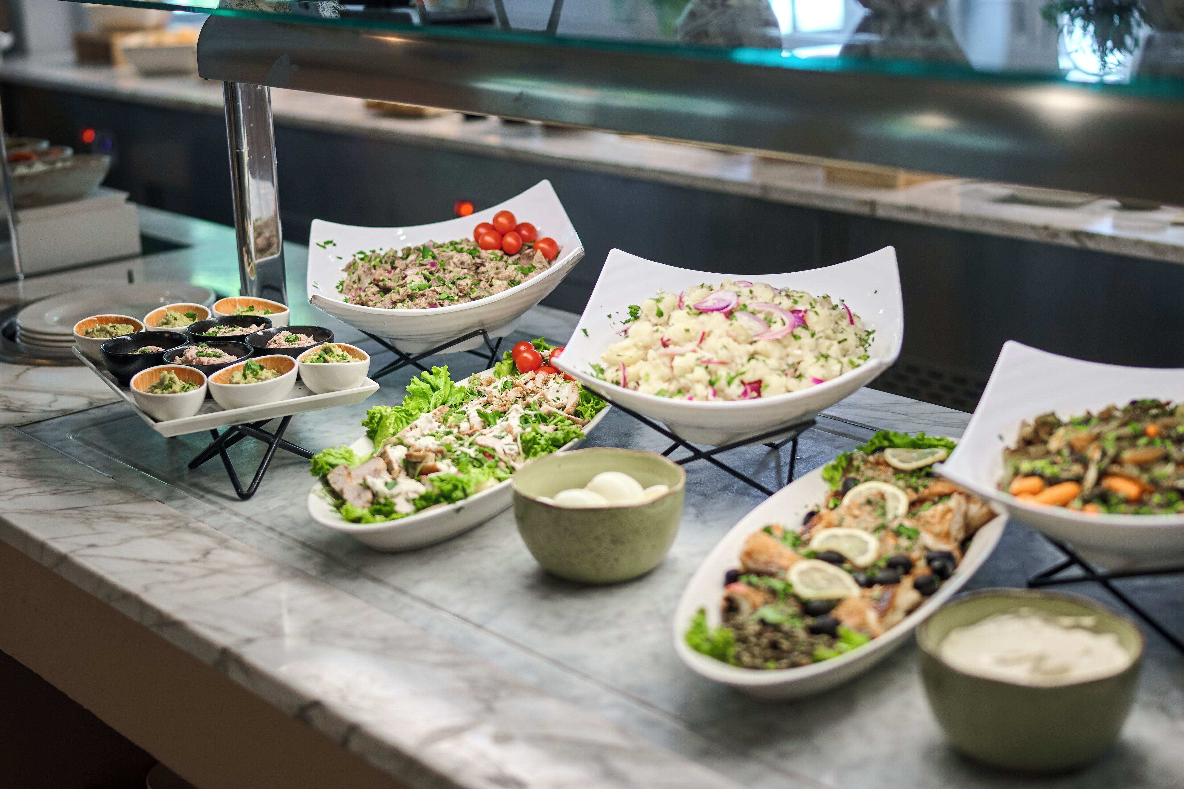 Ein Buffet mit verschiedenen Speisen, darunter Salate, Schalen mit Essen und kleinen Tassen.