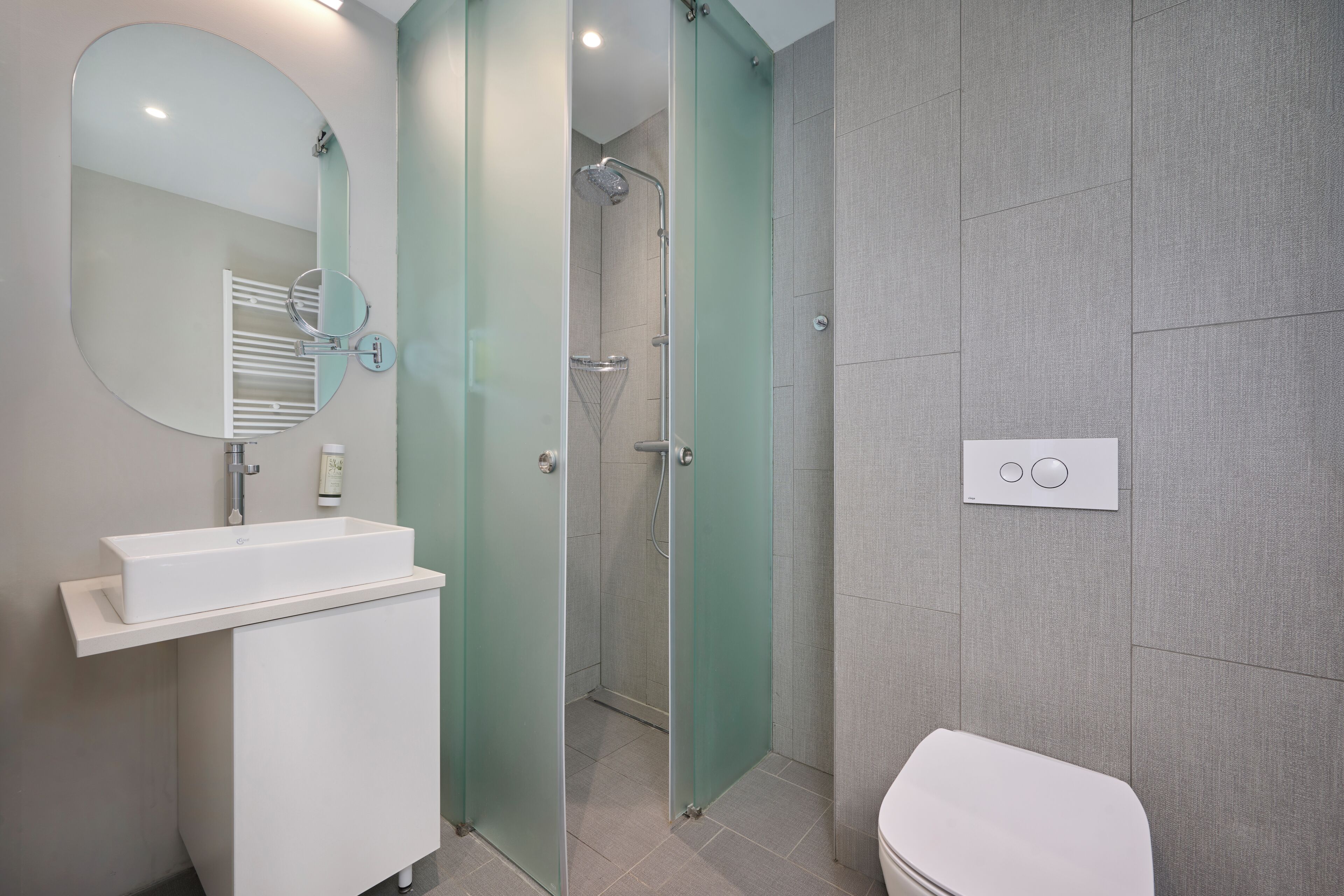 Un baño moderno con lavamanos, espejo y retrete blancos.