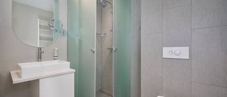 Un baño moderno con lavamanos, espejo y retrete blancos.