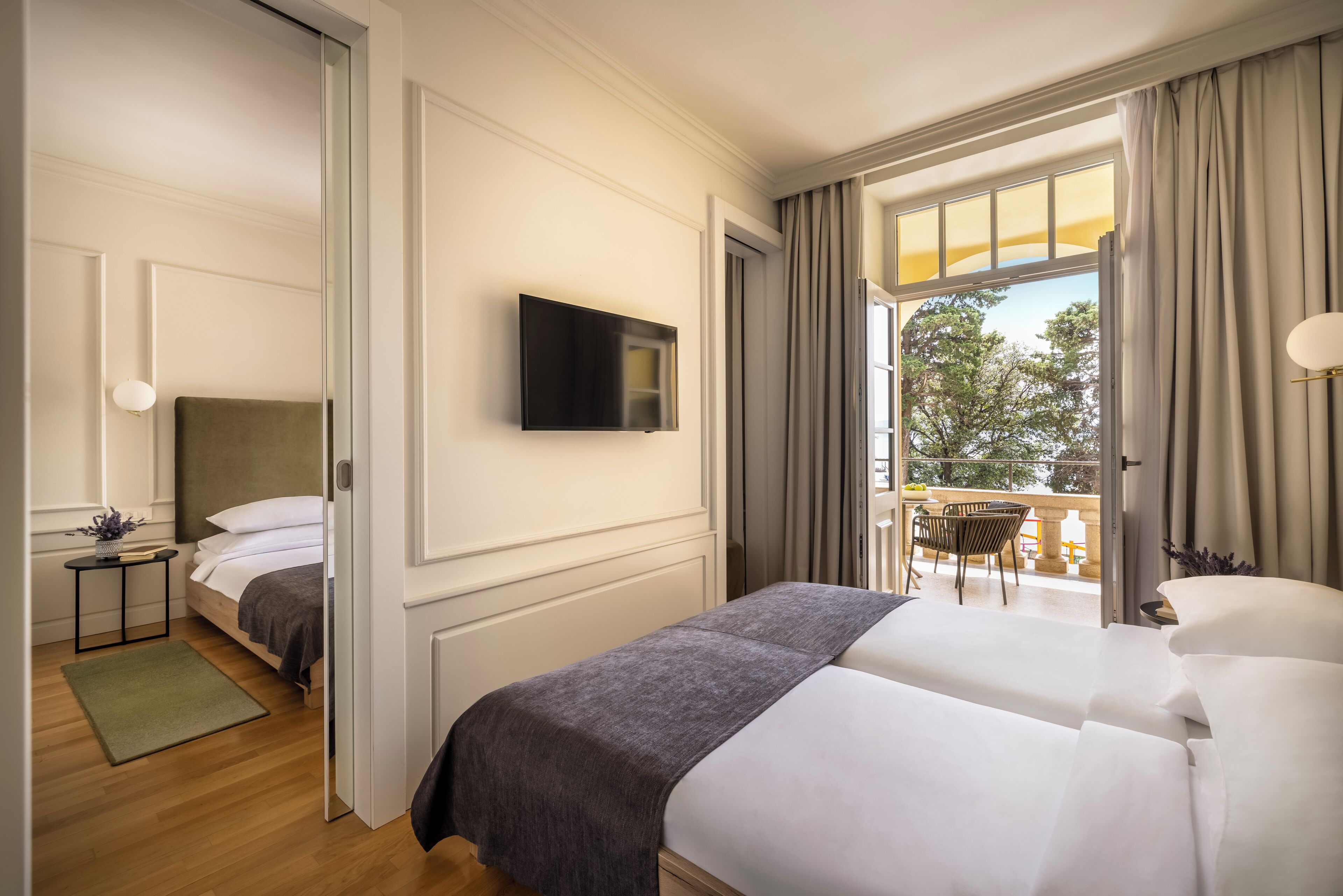 Ett hotellrum med en säng, en tv, ett litet bord med en lampa och utsikt över omgivningarna.
